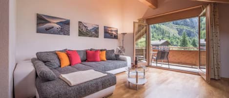 A modern living room with a sofa, a glass coffee table, and a view of a balcony with a wooden deck.
