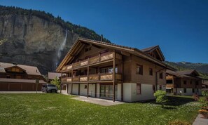 A chalet-style building with a balcony, situated in a mountainous area with a visible waterfall in the background. - SERENE ALPINE PENTHOUSE WITH SPECTACULAR VIEWS (Lauterbrunnen)