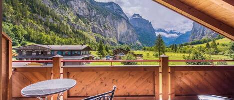 A wooden deck with a table and chairs, overlooking a mountainous landscape with a building labeled 'Karl Brunner Zimmerle Chaletsbau'.