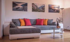 A modern living room with a grey sofa, colorful cushions, a glass coffee table, and three landscape paintings on the wall. - SERENE ALPINE PENTHOUSE WITH SPECTACULAR VIEWS (Lauterbrunnen)