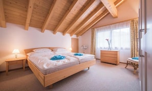 A bedroom with a wooden bed, a nightstand, a dresser, and a window with curtains. - SERENE ALPINE PENTHOUSE WITH SPECTACULAR VIEWS (Lauterbrunnen)