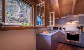 A modern kitchen with a large window, stainless steel appliances, and a view of a mountainous landscape. - SERENE ALPINE PENTHOUSE WITH SPECTACULAR VIEWS (Lauterbrunnen)