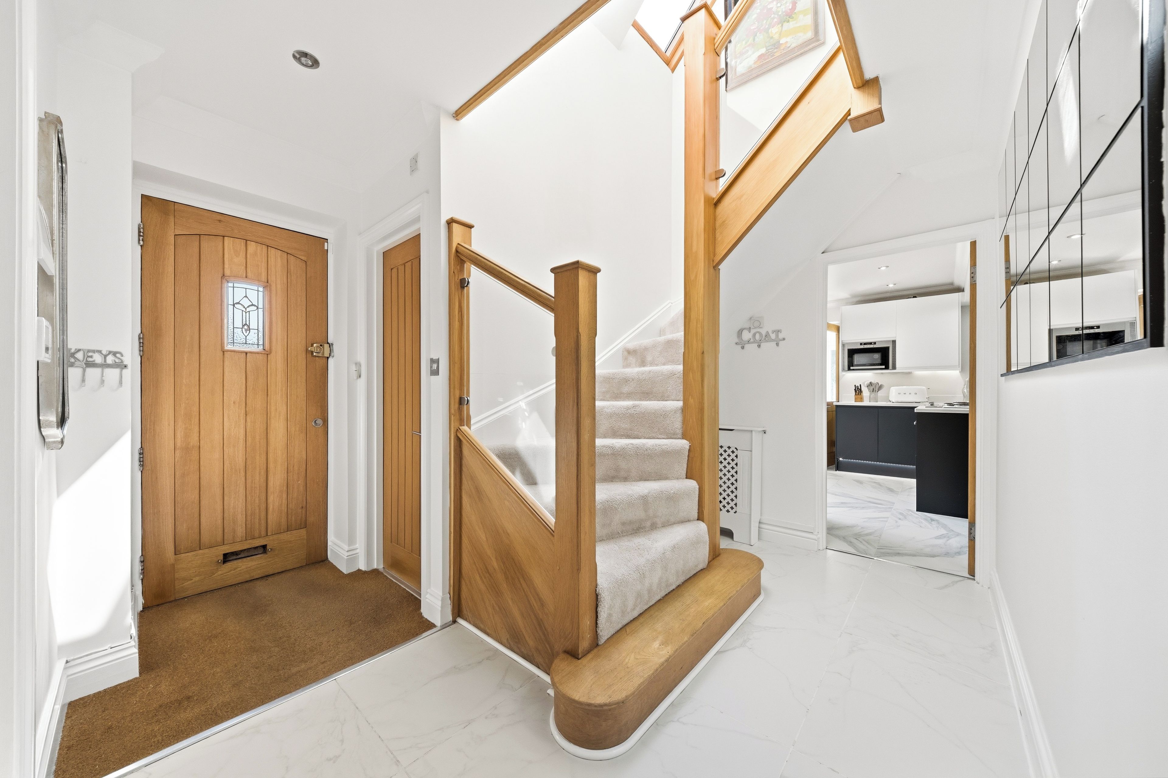 A modern interior with a wooden staircase, a kitchen area, and a door with a key holder.