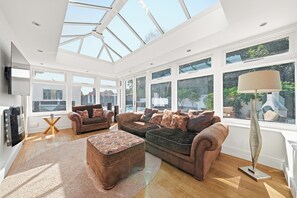 A spacious living room with a high ceiling, large windows, and a central seating area with sofas and a coffee table. - Cedars Bournemouth Pool, hot Tub, Sleep 8,by Carly (Bournemouth)
