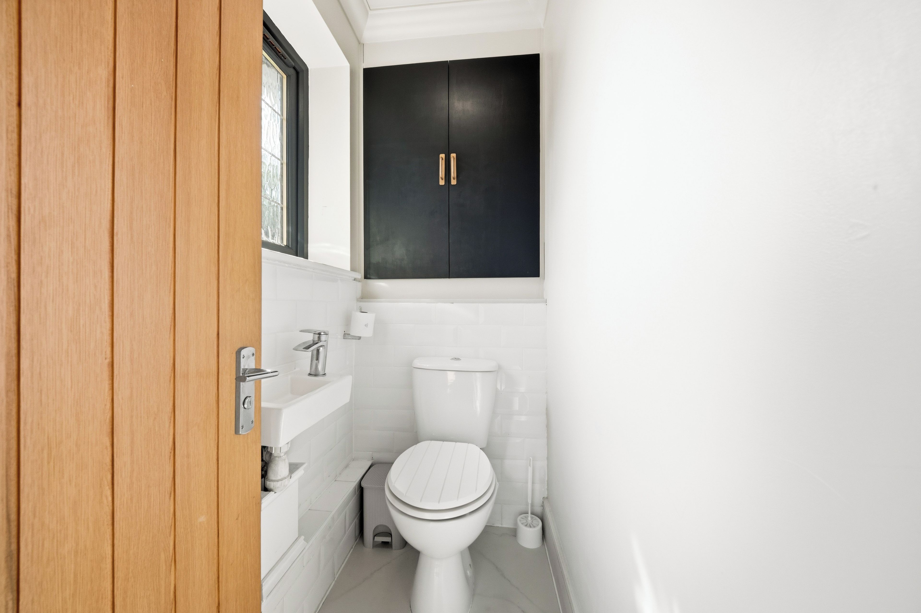 A bathroom with a white toilet, a small step stool, and a black cabinet above the sink.