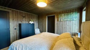 Ein Schlafzimmer mit Bett, Kleiderschrank, Tür und Fenster mit Blick auf Bäume.