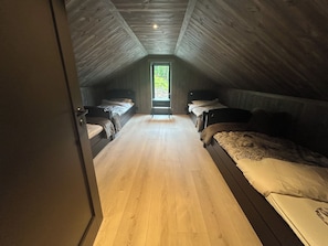 A bedroom with two beds, wooden flooring, and a window at the far end.