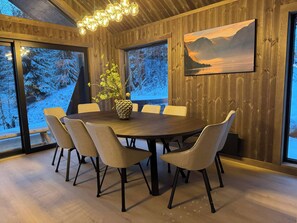 Ein Essbereich mit einem runden Tisch, sechs Stühlen, einer Blumenvase, Holzwänden und einem Gemälde einer Berglandschaft.