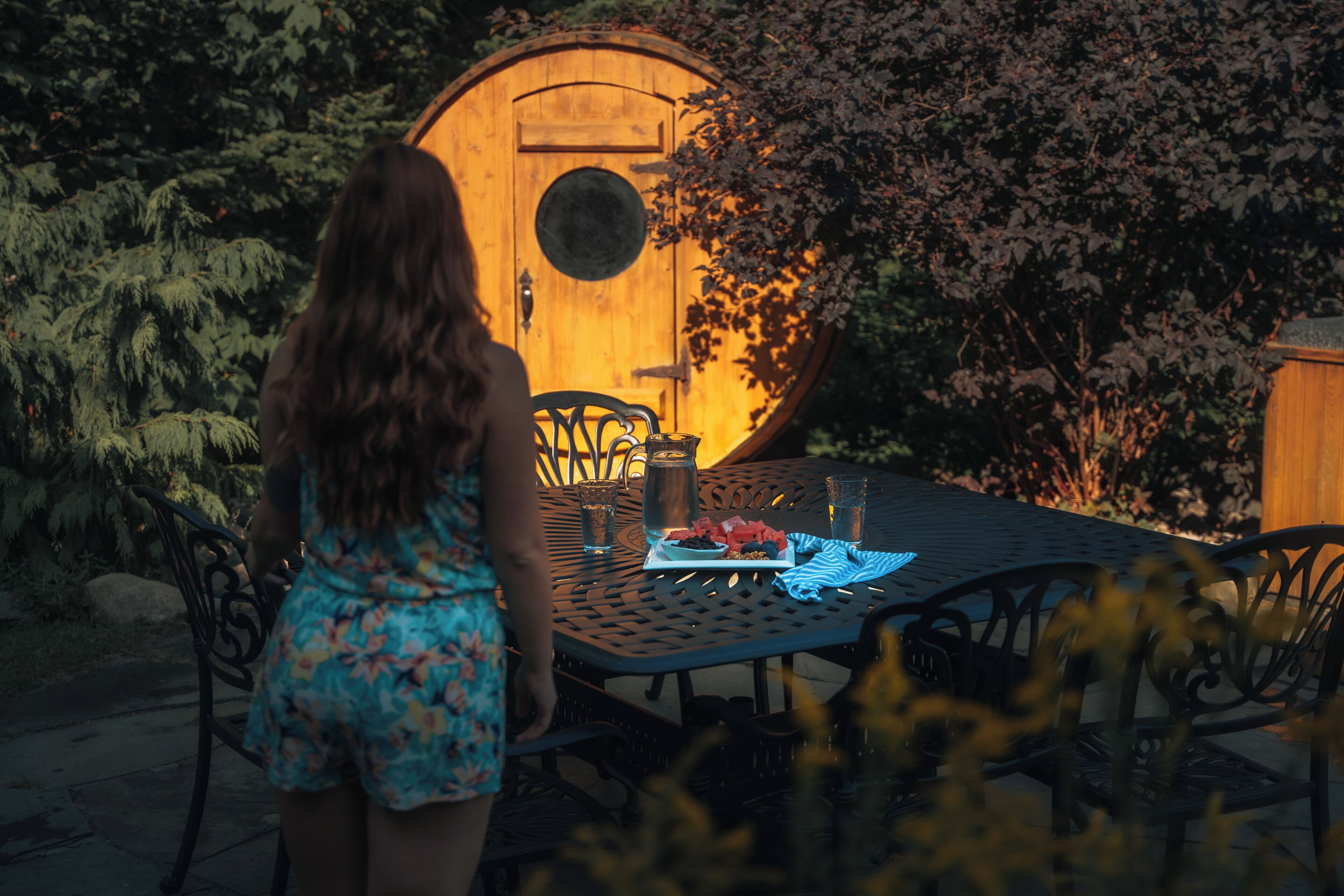A woman standing at a table with a wooden barrel structure in the background.