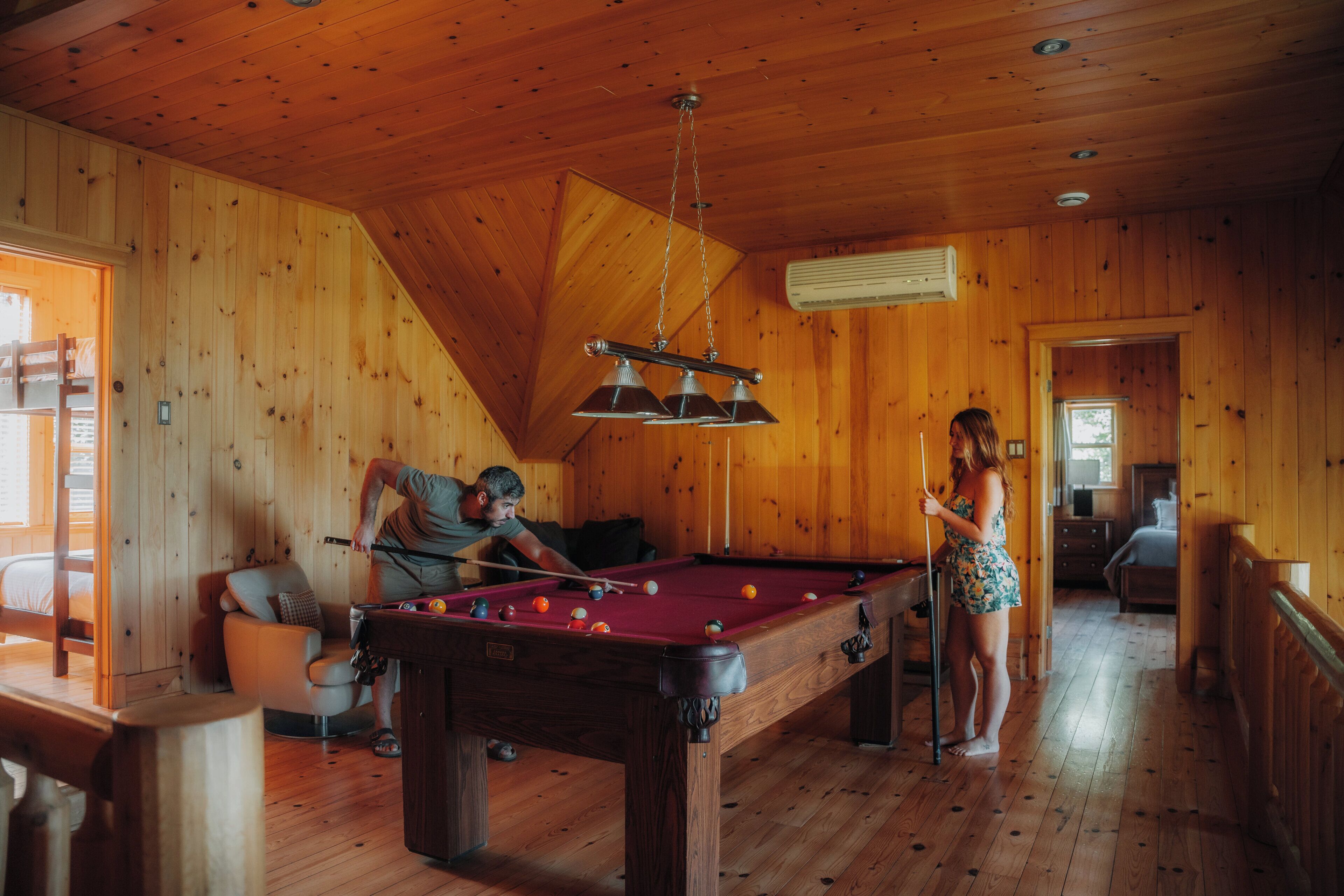 Une pièce en bois avec une table de billard, un canapé et une personne qui joue au billard.