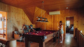 Une pièce en bois avec une table de billard, un canapé et une personne qui joue au billard.