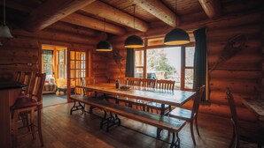 A wooden cabin interior with a large dining table, benches, and hanging pendant lights. - LUXURY LOG CABIN (Mille-Isles)