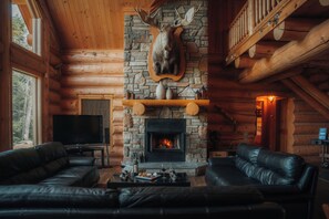 A log cabin interior with a stone fireplace, leather sofas, and a mounted deer head. - LUXURY LOG CABIN (Mille-Isles)