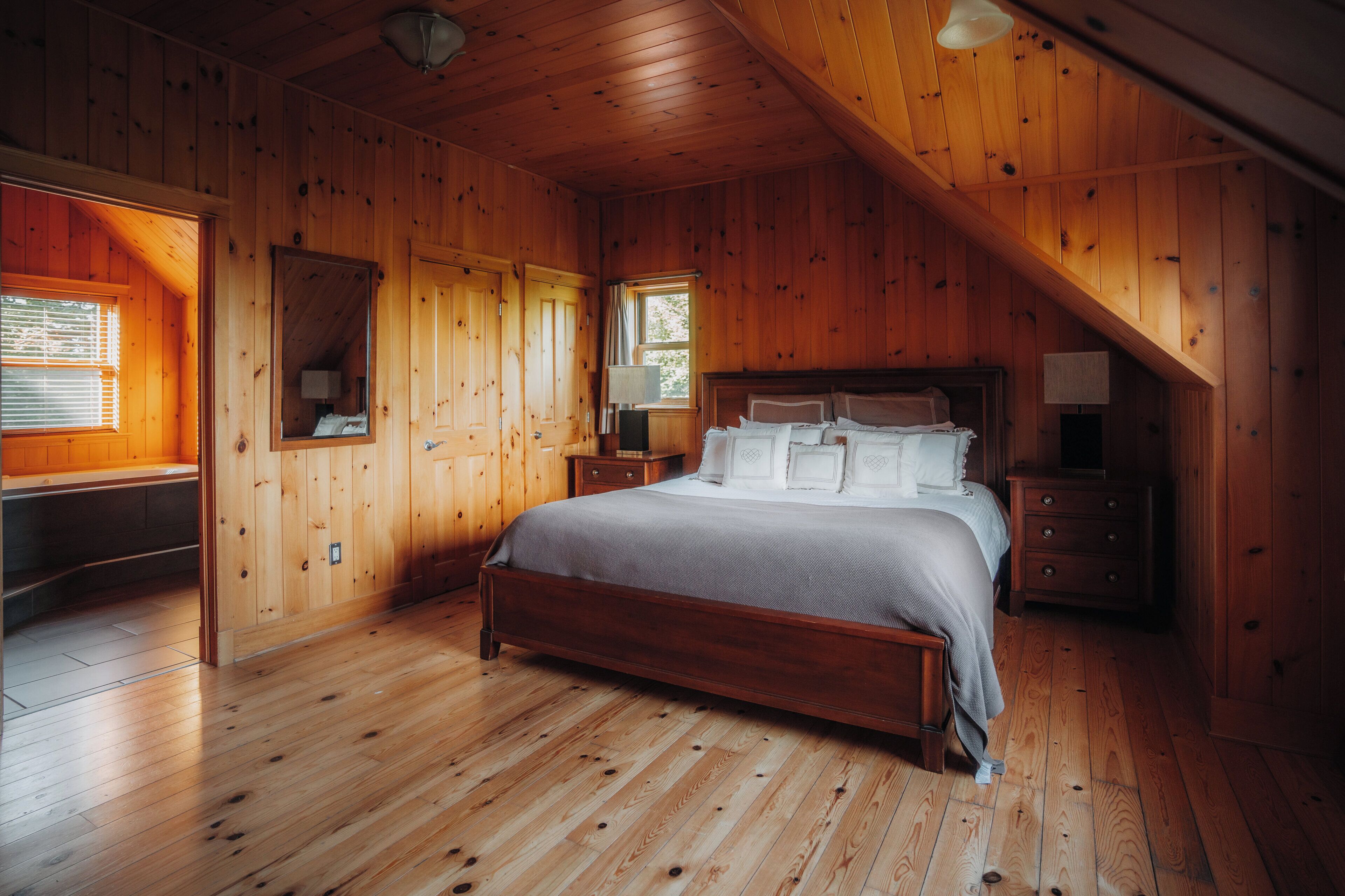 Une chambre à coucher aux murs lambrissés, avec un lit, des tables de chevet, un miroir et une fenêtre.