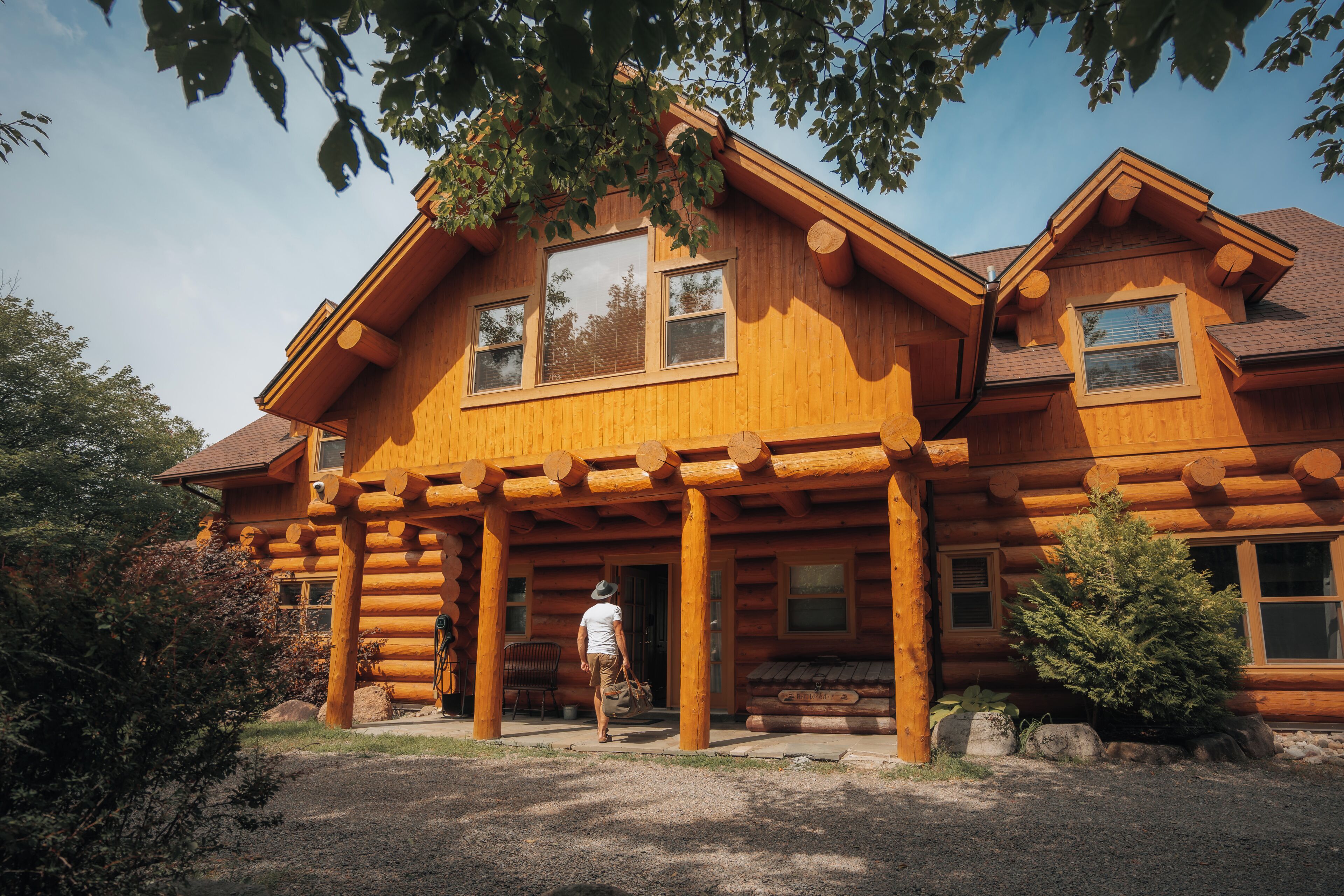 Une cabane en rondins dotée d’une véranda, de grandes fenêtres et de fondations en pierre.