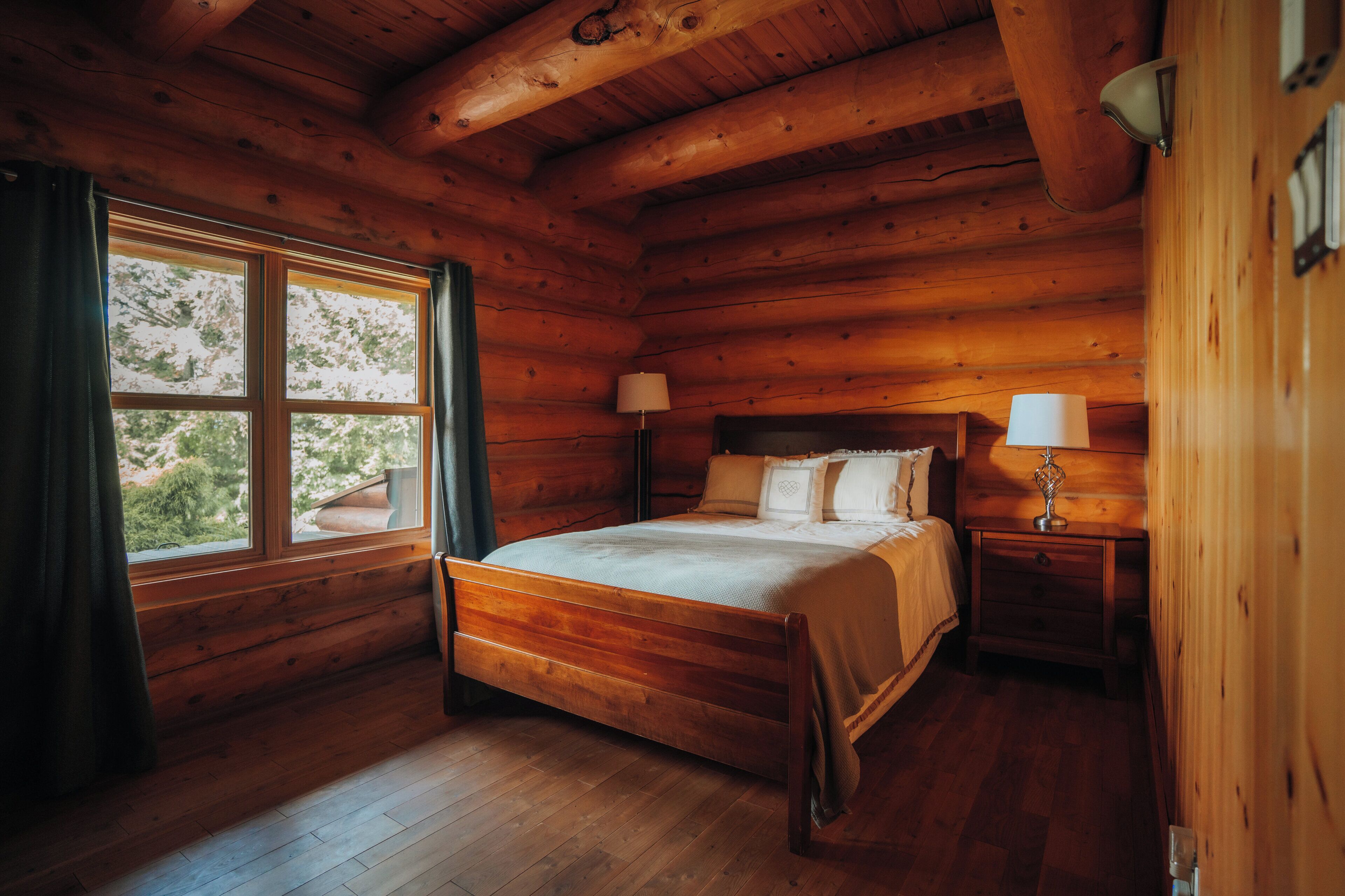 Une chambre à coucher dans une cabane en bois, avec un lit à baldaquin, deux lampes de chevet et une fenêtre avec des rideaux.
