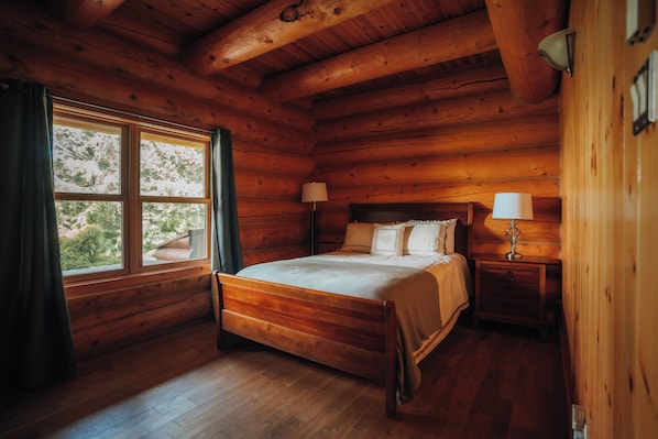 A wooden cabin bedroom with a four-poster bed, two bedside lamps, and a window with curtains.