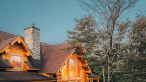 A log cabin with a stone chimney, a porch, and a well-maintained lawn. - LUXURY LOG CABIN (Mille-Isles)