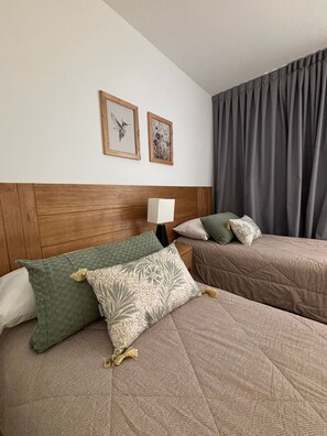 Een hotelkamer met twee bedden, een houten hoofdbord, een nachtkastje met lamp en twee ingelijste foto's aan de muur.