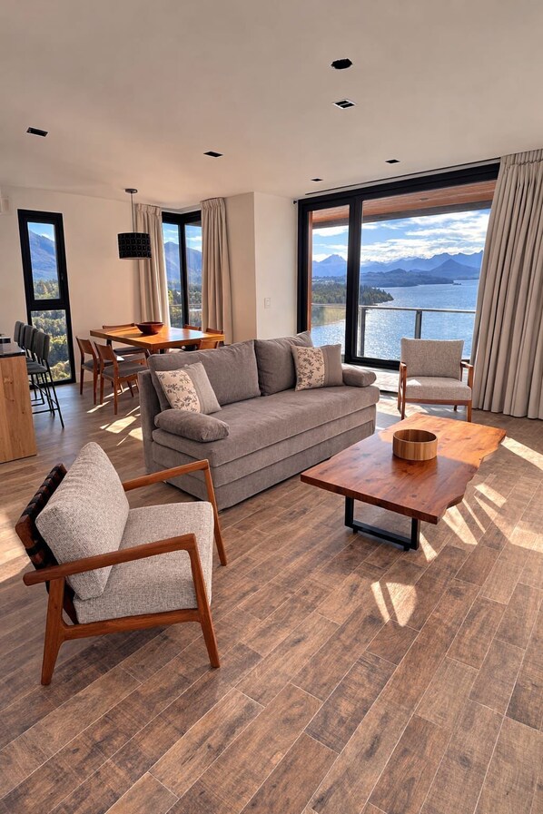 Un salon moderne avec un canapé, des fauteuils, une table à manger et une vue sur un lac et des montagnes.