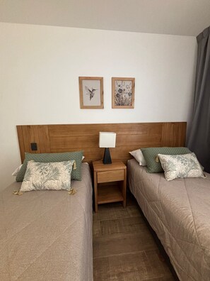 Ein Hotelzimmer mit zwei Betten, einem Nachttisch mit Lampe und zwei gerahmten Bildern an der Wand.
