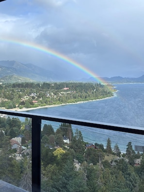 Un paysage côtier avec un arc-en-ciel, des maisons et une zone boisée.