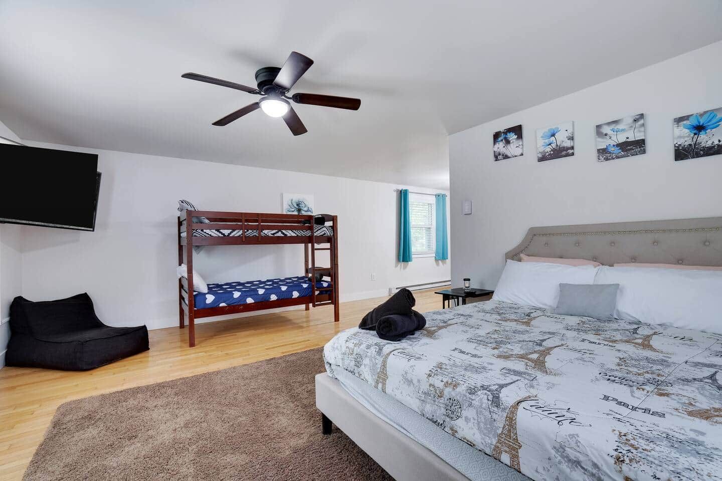 A bedroom with a bunk bed, a single bed, a ceiling fan, a TV, and artwork on the wall.