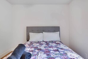 A bed with a floral bedspread and two pillows, a grey headboard, and a rolled-up grey blanket on the floor. - Ultimate Pocono Getaway | HotTub•Theater•GameRoom (Tunkhannock Township)