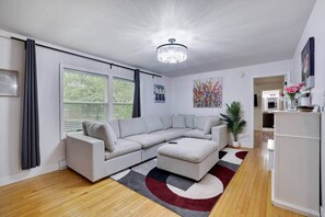 A modern living room with a sectional sofa, a chandelier, and a view of the outdoors through large windows. - Ultimate Pocono Getaway  HotTub•Theater•GameRoom (Tunkhannock Township)