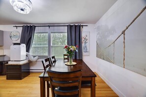 A dining area with a wooden table, chairs, a vase of flowers, a clock, and a large window with curtains. - Ultimate Pocono Getaway | HotTub•Theater•GameRoom (Tunkhannock Township)