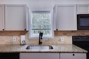 A kitchen with a granite countertop, stainless steel sink, white cabinets, and a window with blinds. - Ultimate Pocono Getaway | HotTub•Theater•GameRoom (Tunkhannock Township)