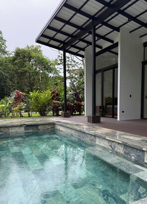 A swimming pool with a covered area, surrounded by lush greenery and a modern building with large windows. - Villa Azur 1 - New 3-bedroom with Arenal views, pool, rainforest in La Fortuna (La Fortuna)