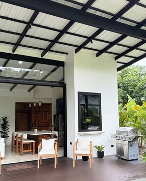 A modern kitchen with a large island, a dining area with chairs, a grill, and a view of greenery. - Villa Azur 1 - New 3-bedroom with Arenal views, pool, rainforest in La Fortuna (La Fortuna)