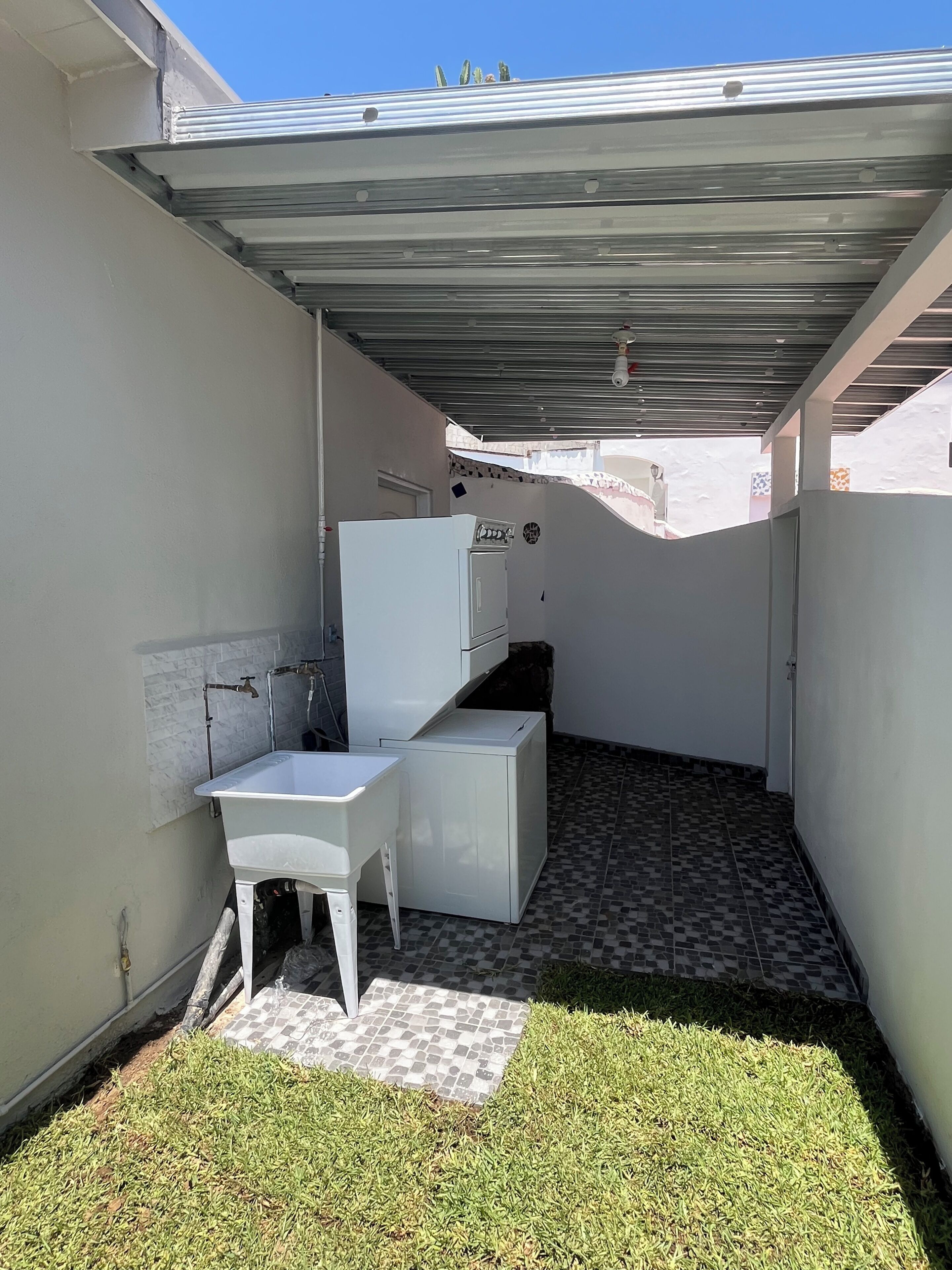 Un petit espace extérieur clos, comprenant un coin lavabo blanc, une petite table et un sol carrelé.