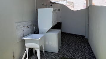 Un petit espace extérieur clos, comprenant un coin lavabo blanc, une petite table et un sol carrelé.