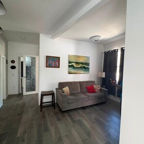 A living room with a grey sofa, a small table, and two paintings on the wall. - CasitaRosarito Parking & Quick Highway access (playas de Rosarito)