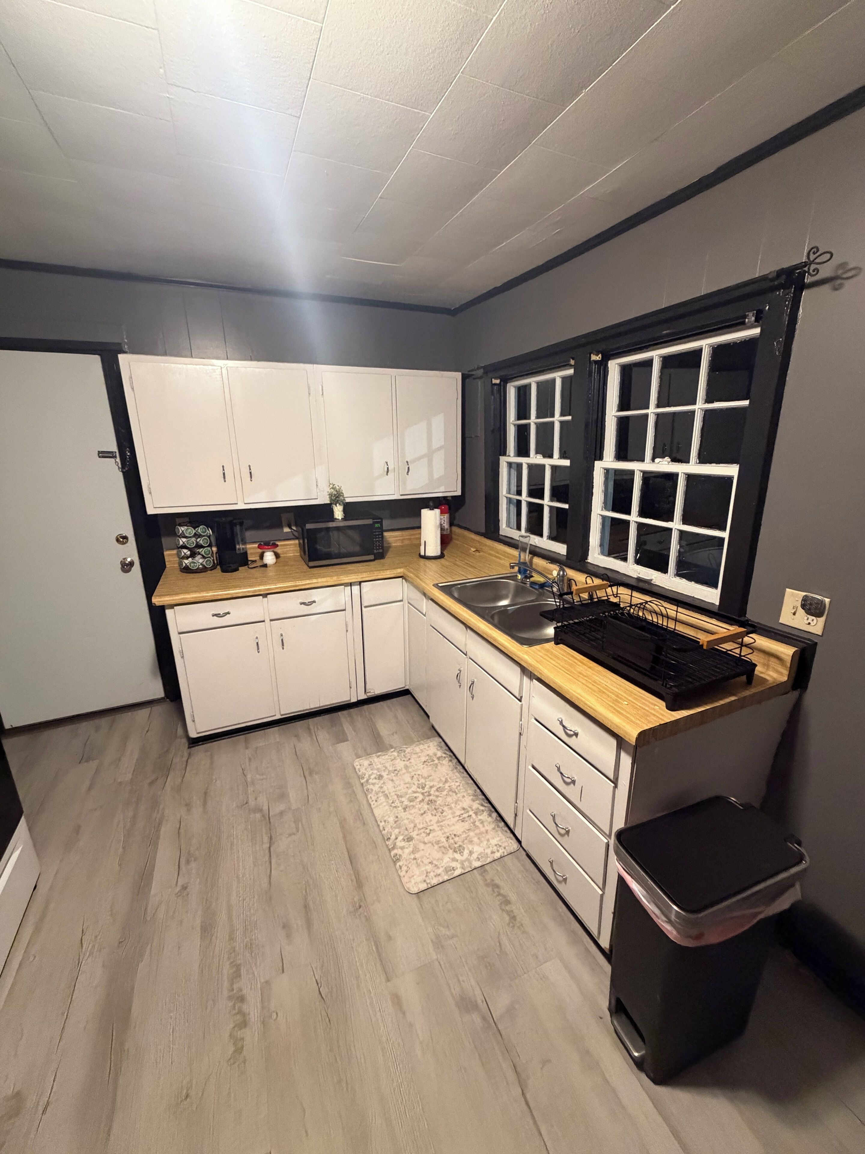 Una cocina compacta con armarios blancos, encimera de madera, microondas y lavabo.