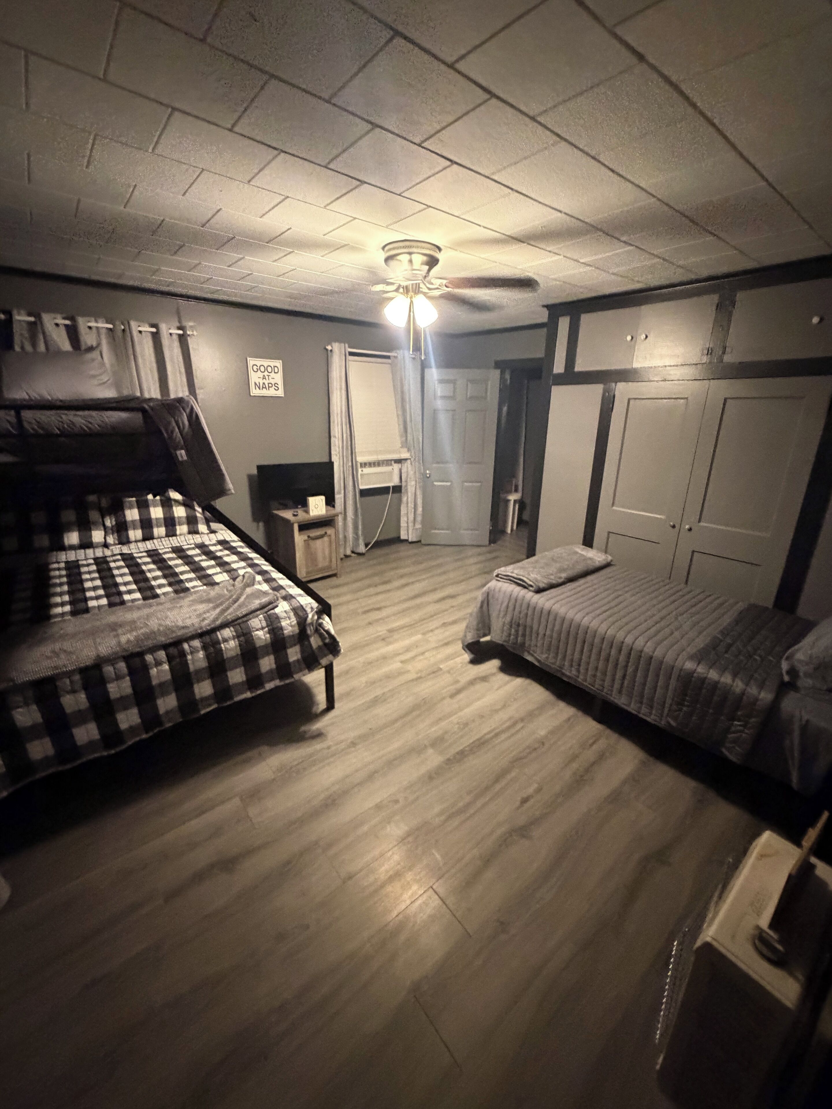 Una habitación con dos camas, ventilador de techo, una puerta y una mesita.