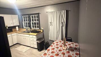 A compact kitchen with white cabinets, a microwave, and a sink. There's a dining table with a floral tablecloth.
