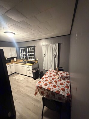 A compact kitchen with white cabinets, a microwave, and a sink. There's a dining table with a floral tablecloth.