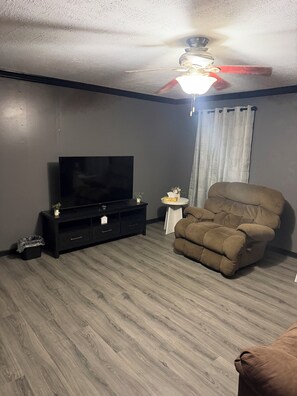 A living room with a dark wood floor, a black entertainment unit, a brown recliner, and a ceiling fan. - The Willow at Toomsuba (Toomsuba)