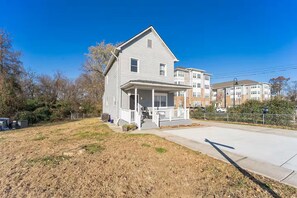 A two-story residential building with a front porch, a garage, and a small front yard. - 4-bedroom house in tranquil Baltimore Highlands with AC (Baltimore Highlands)
