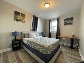 A hotel room with a bed, bedside tables, a desk, and a window. - 4-bedroom house in tranquil Baltimore Highlands with AC (Baltimore Highlands)