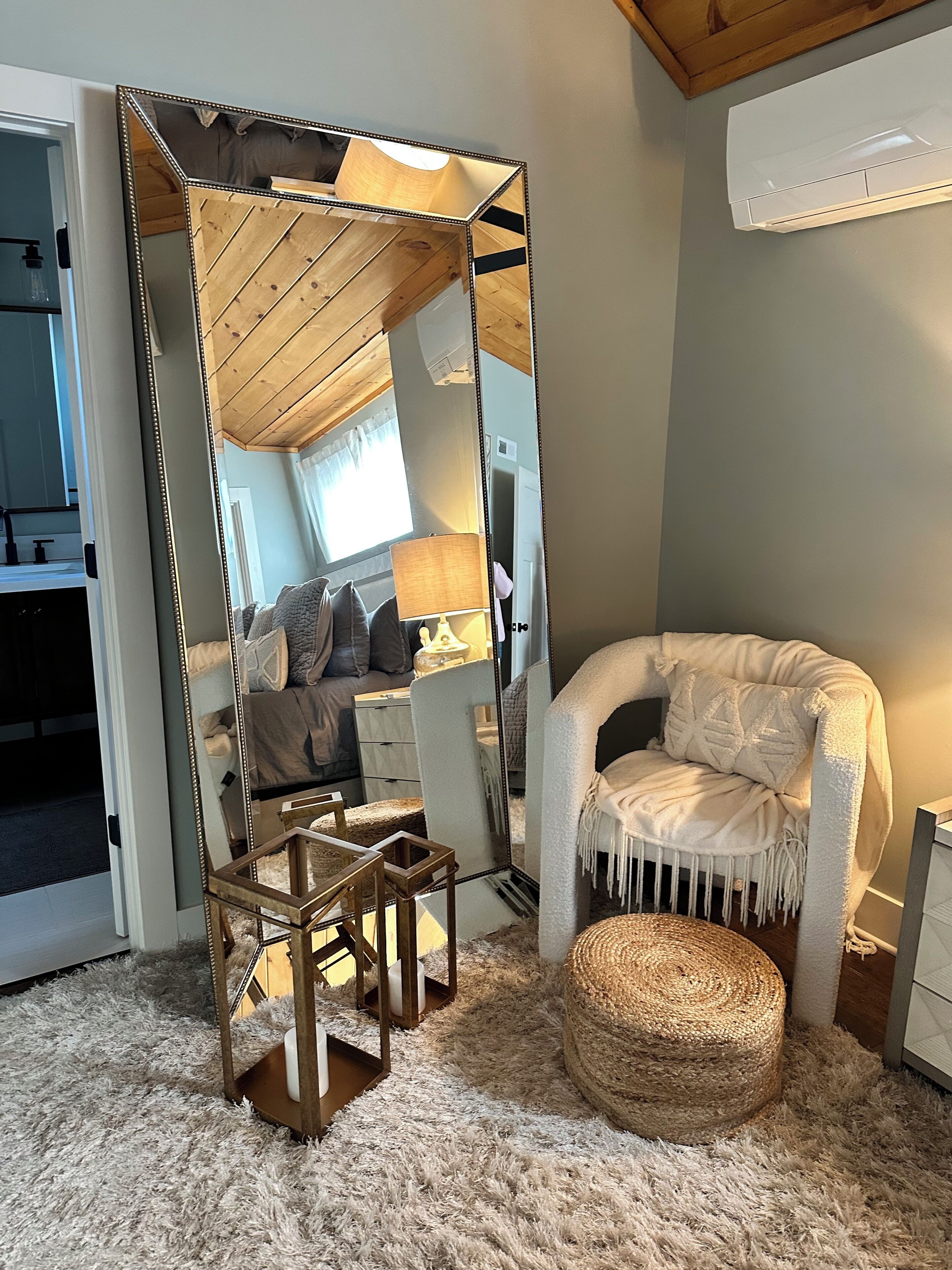 Une pièce chaleureuse avec un grand miroir, un canapé confortable, une petite table en bois et un pouf décoratif.