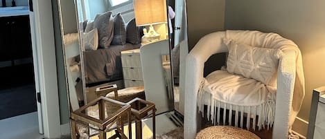 Una habitación acogedora con un espejo grande, un sofá cómodo, una mesita de madera y un pouf decorativo.