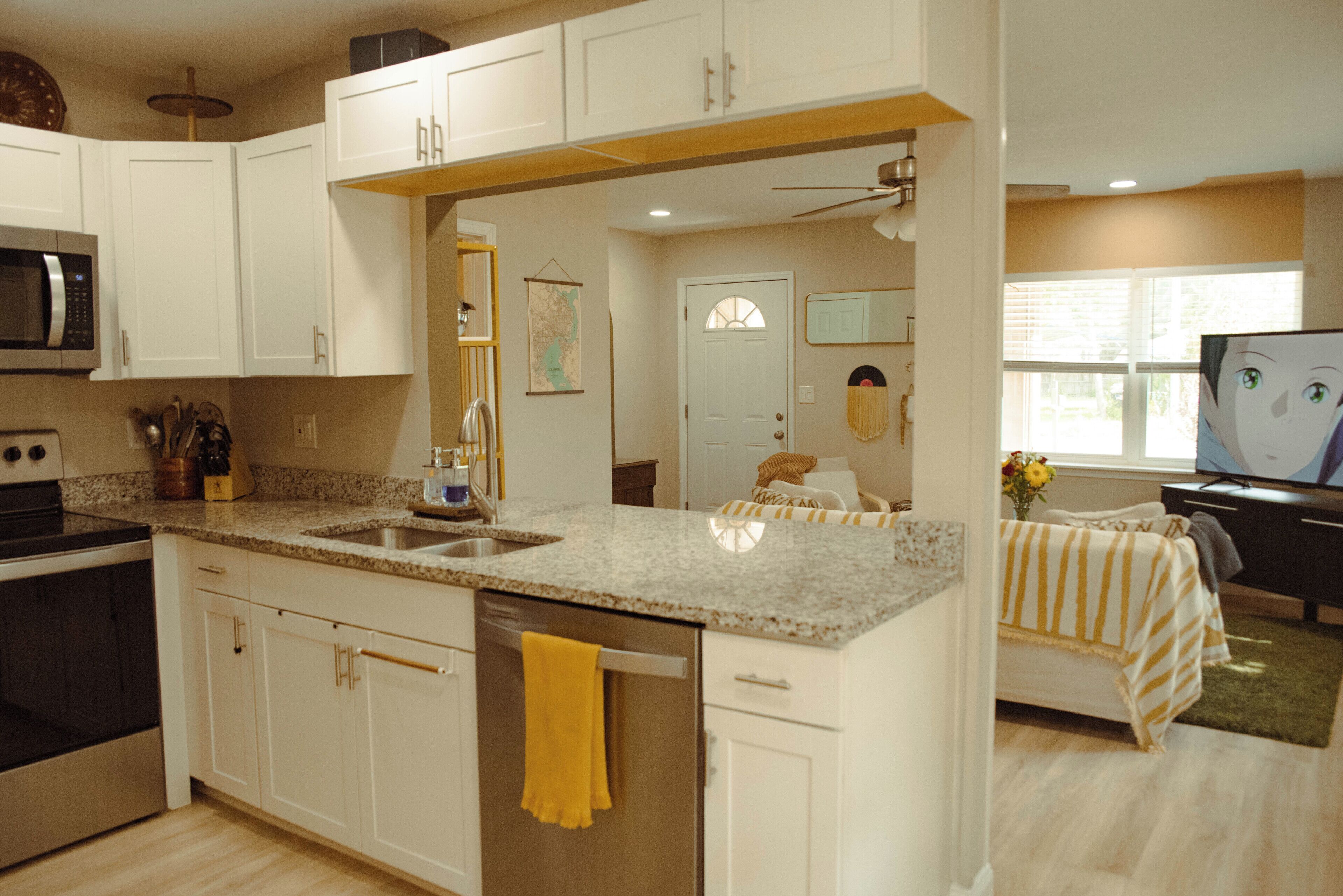 A kitchen with white cabinets, a microwave, a sink, and a yellow towel hanging on the door.