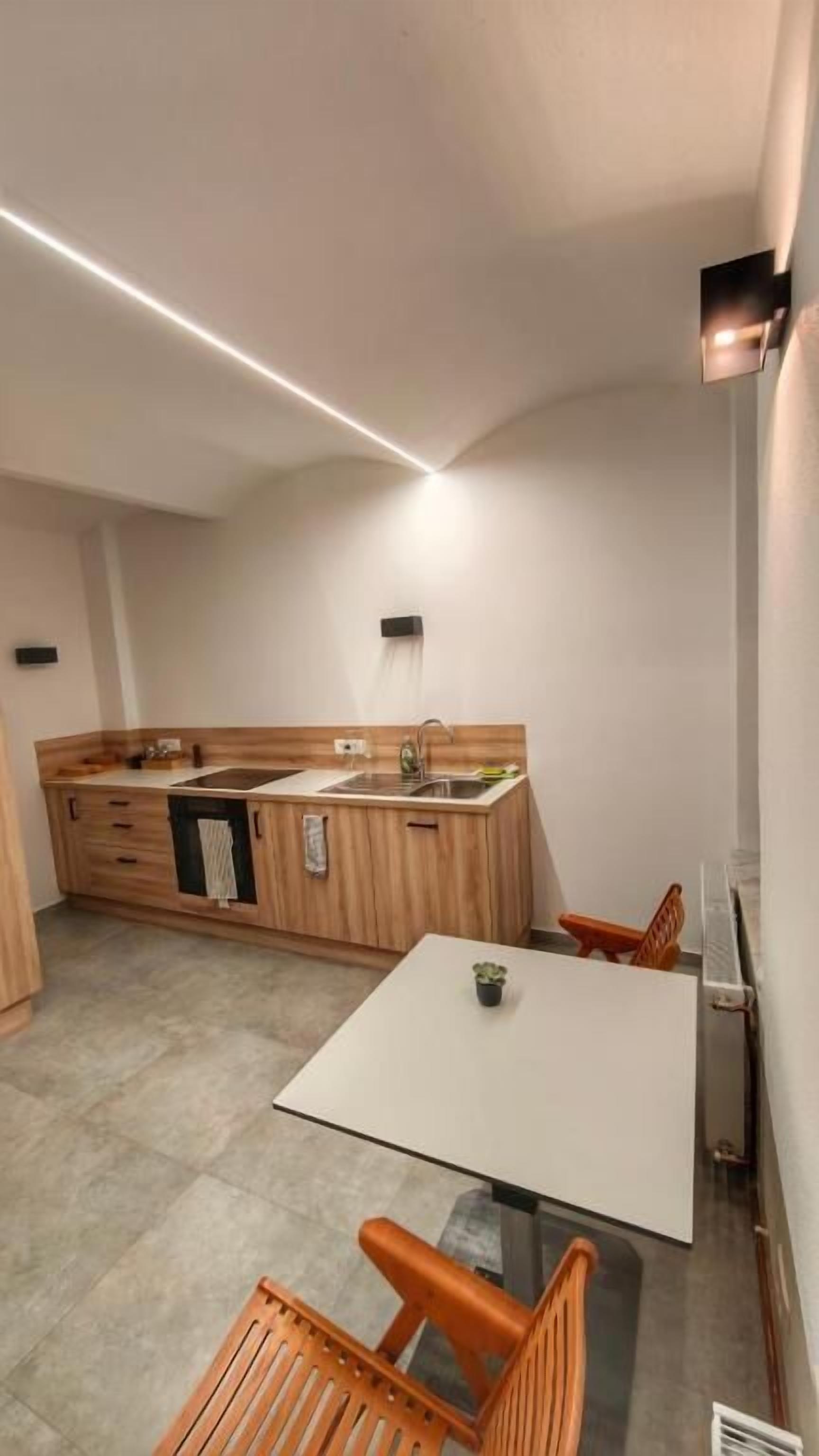 Eine kompakte Küche mit Holzschränken, einer weißen Arbeitsplatte und einem Essbereich mit Tisch und Stühlen.