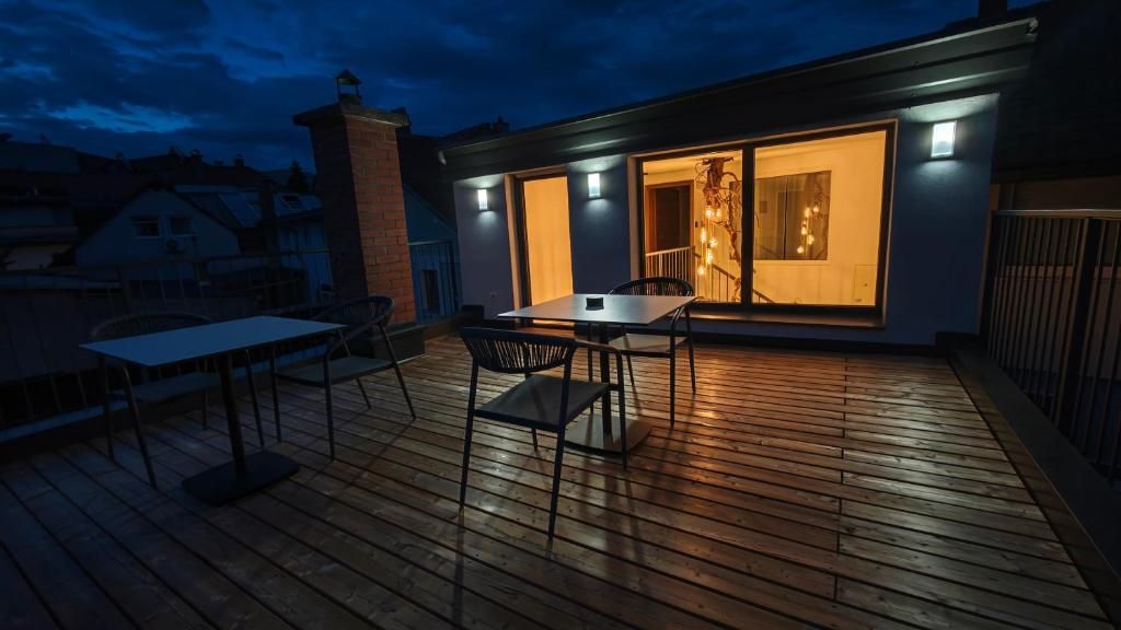 Eine Holzterrasse mit Tisch und Stühlen, ein Backsteinsschornstein und ein modernes Gebäude mit großen Fenstern.