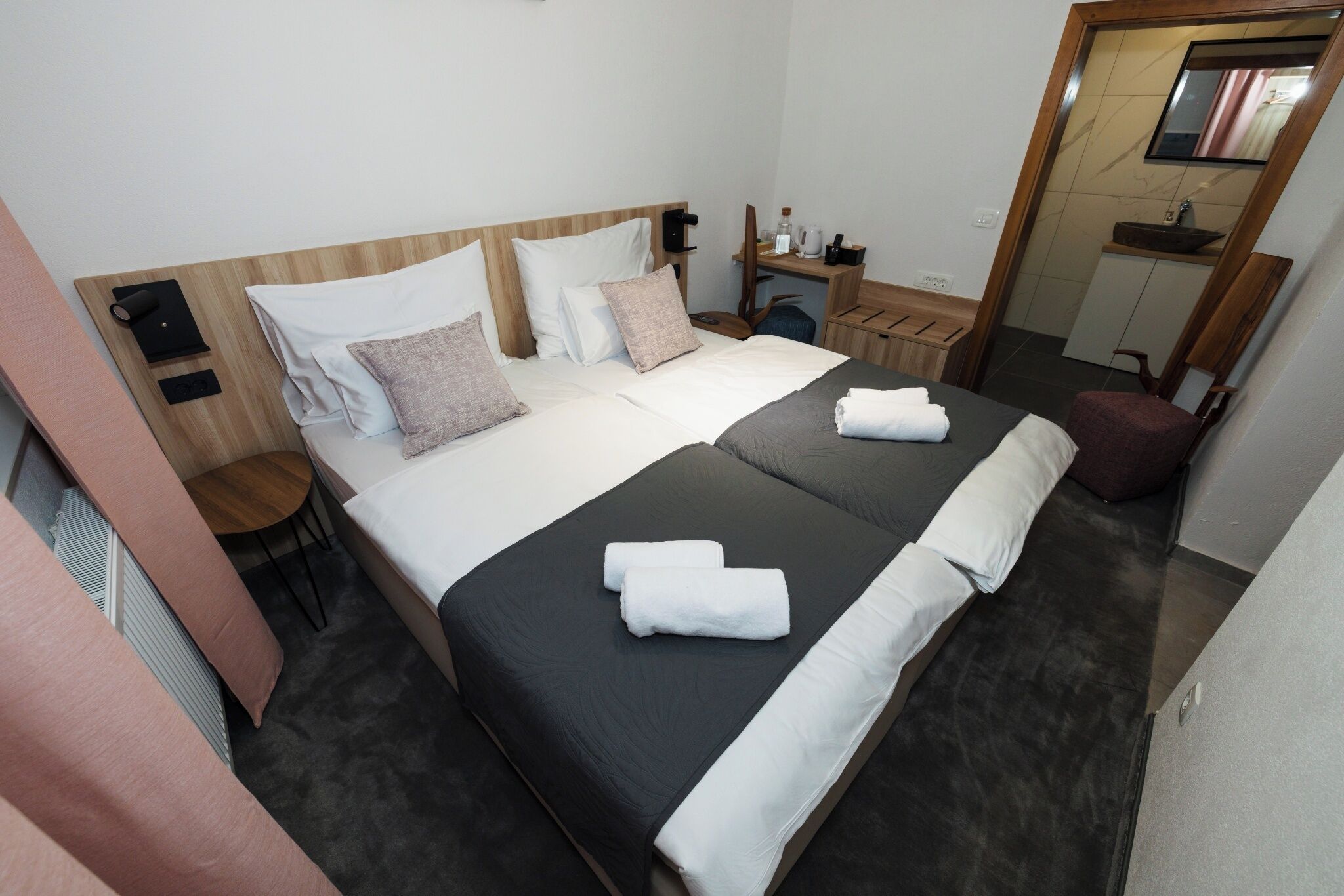 A double bed with two pillows, a bedside table, a mirror, and a small stool.