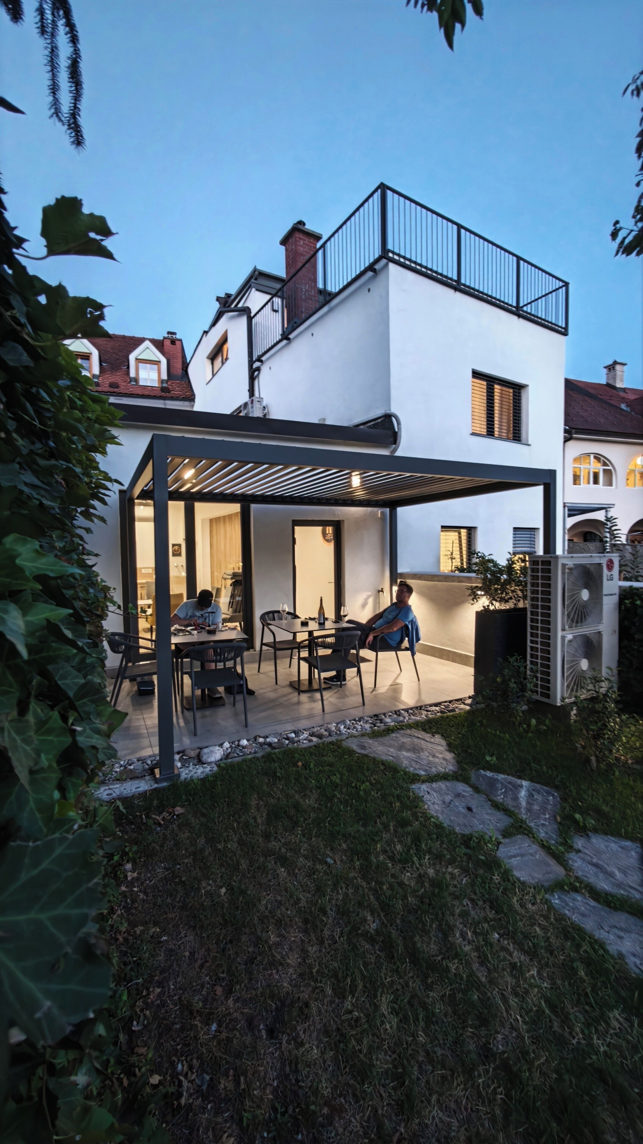 A modern outdoor patio with a pergola, seating, and a person working at a table.
